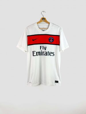 Vue de face du maillot extérieur PSG 2011-2012 (modèle Pastore #27) : tunique blanche à bande rouge horizontale sur la poitrine, avec logo Nike, sponsor Fly Emirates et blason PSG 1970.