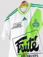 Détail du logo AS Saint-Étienne et du col rond du maillot domicile 2009-2010, finition Adidas, sur fond blanc et vert clair.