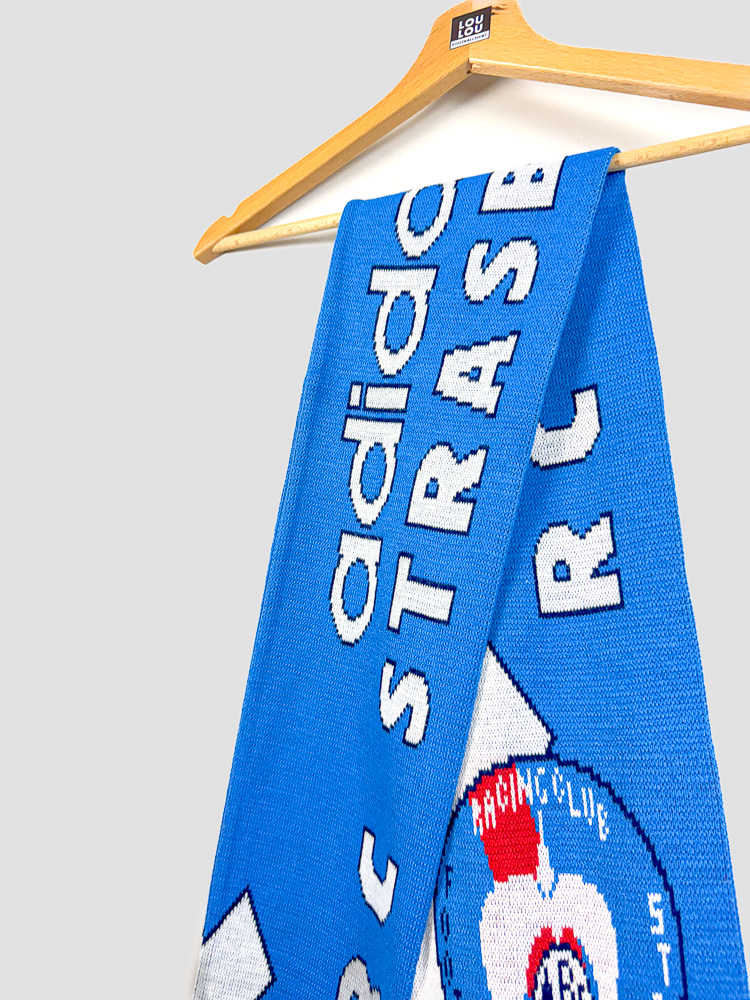 echarpe-collector-rc-strasbourg-1996-1997-gros-plan-logo-adidas-lettrage Gros plan sur l'écharpe RC Strasbourg 1996-1997, lettrage adidas et RC STRASBOURG tissés en blanc sur fond bleu Racing vintage.