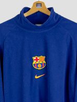 polaire-fc-barcelona-1998-99-col-montant-detail-ecusson-fcb-nike Gros plan sur l'écusson FCB et le logo Nike de la polaire officielle FC Barcelona 1998-1999 en fleece bleu