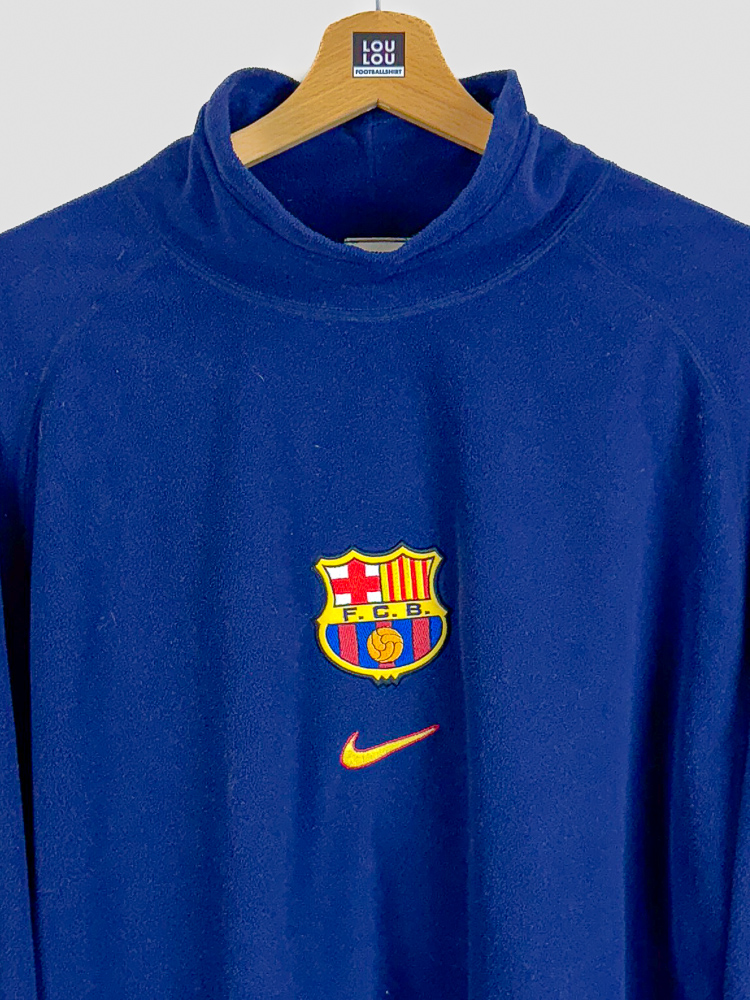 polaire-fc-barcelona-1998-99-col-montant-detail-ecusson-fcb-nike Gros plan sur l'écusson FCB et le logo Nike de la polaire officielle FC Barcelona 1998-1999 en fleece bleu
